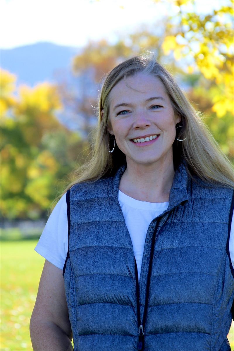 Cindy smiling outdoors in front of autumn trees and mountains